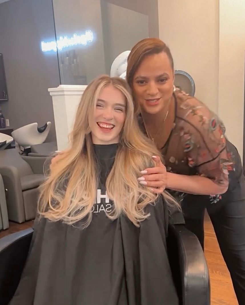 Woman with new hairstyle smiles while hairstylist places hand on her shoulder in a salon.