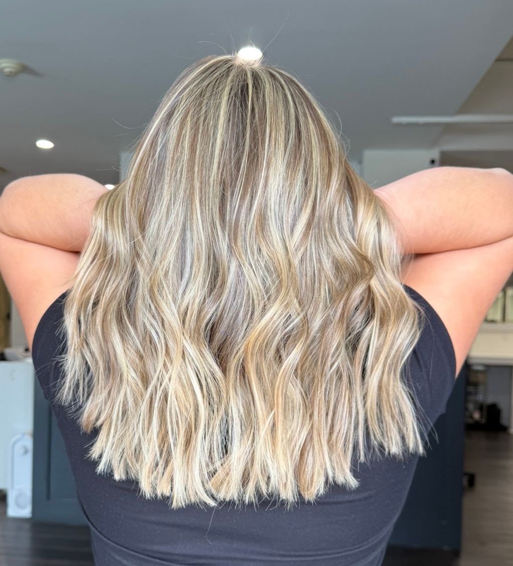 Blonde wavy hair with highlights, styled, against a black shirt, arms crossed.