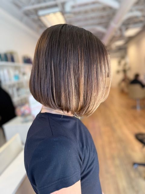 Bob haircut with highlights, featuring dark brown roots and lighter ends, in a salon setting.