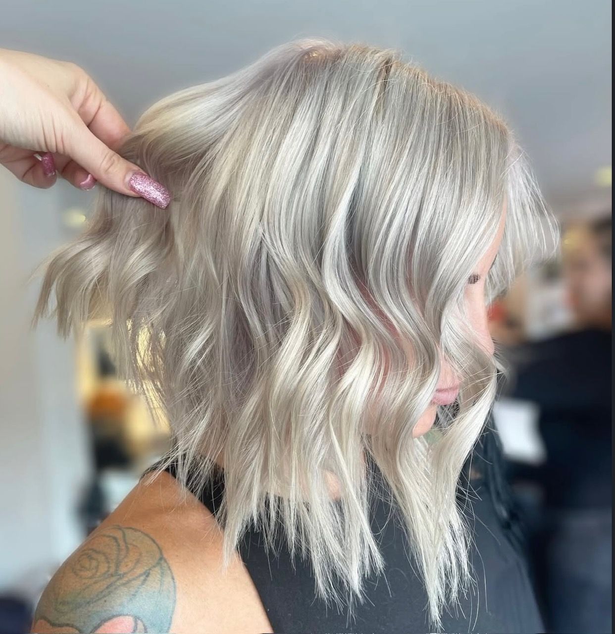 Woman with wavy, light blonde bob hairstyle, getting hair styled by a hand with manicured nails.