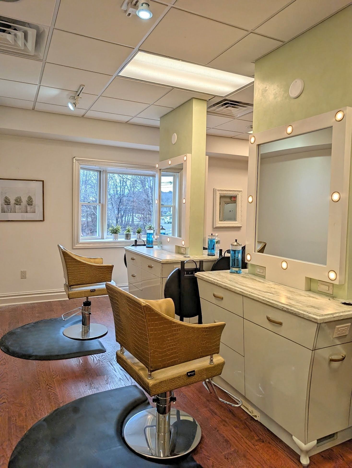 Hair salon interior with two chairs, mirrors, and work stations near a window.