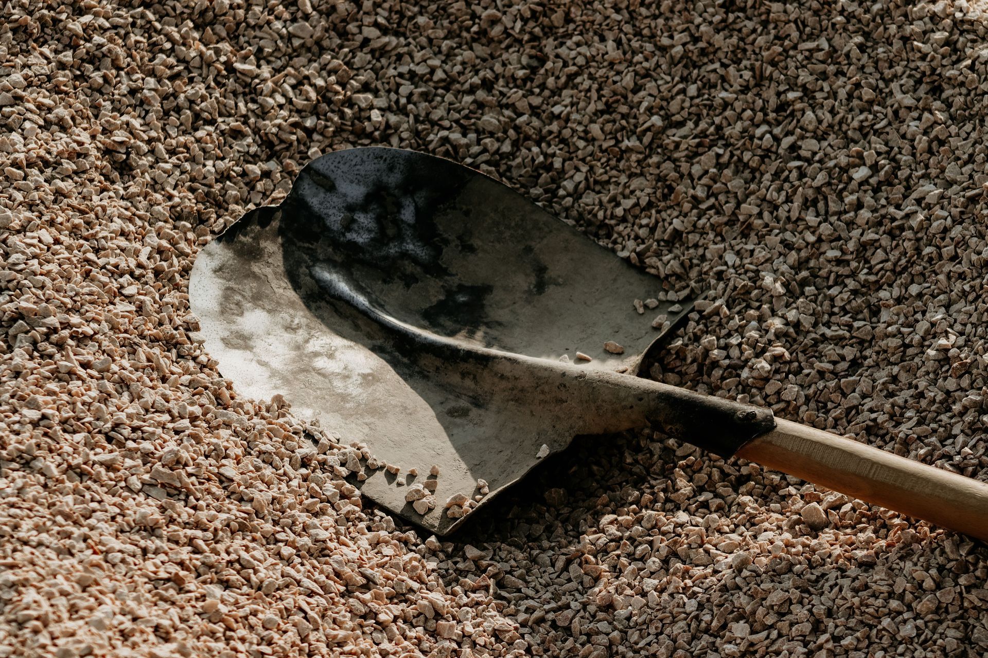 Shovel lifting a scoop of gravel or dirt from a rough, pebbled surface.