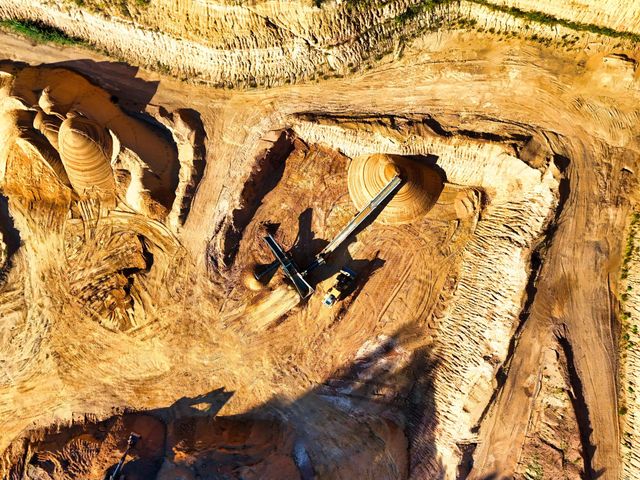 Aerial view of a sandy excavation site with a large drilling machine and tire tracks