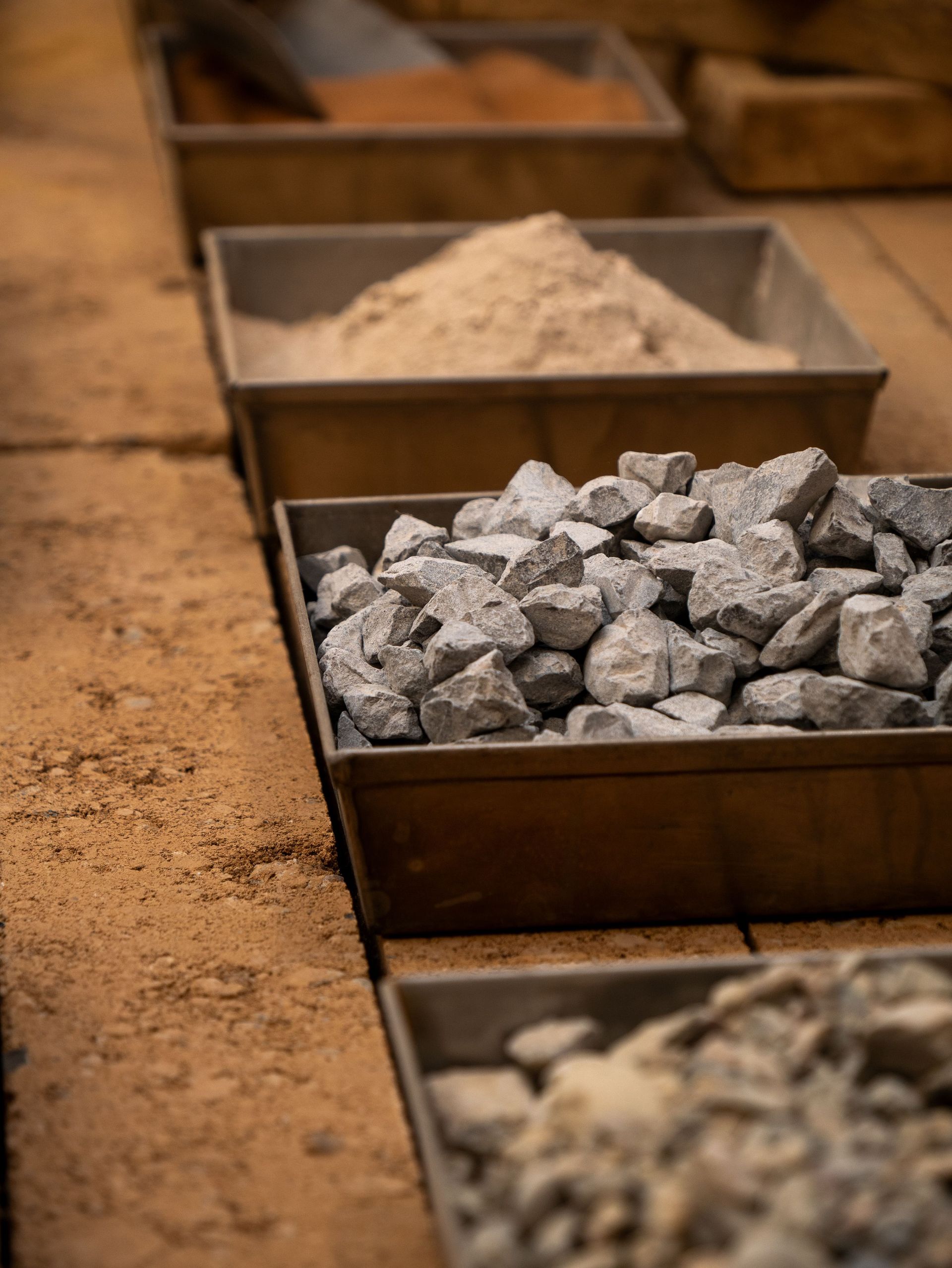 Metal trays of white powder and gray stones on a sandy surface, shallow depth of field.