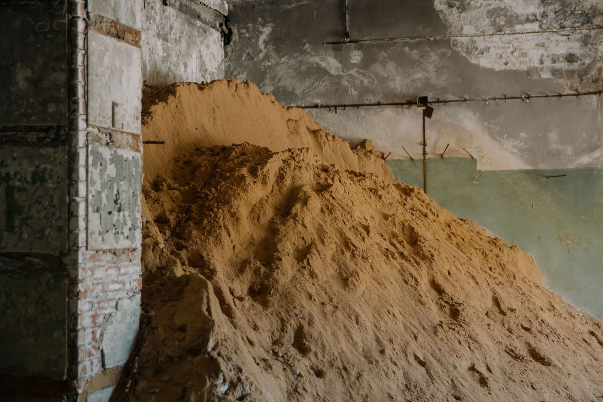 Large pile of sand stacked against a weathered concrete wall in an unfinished room