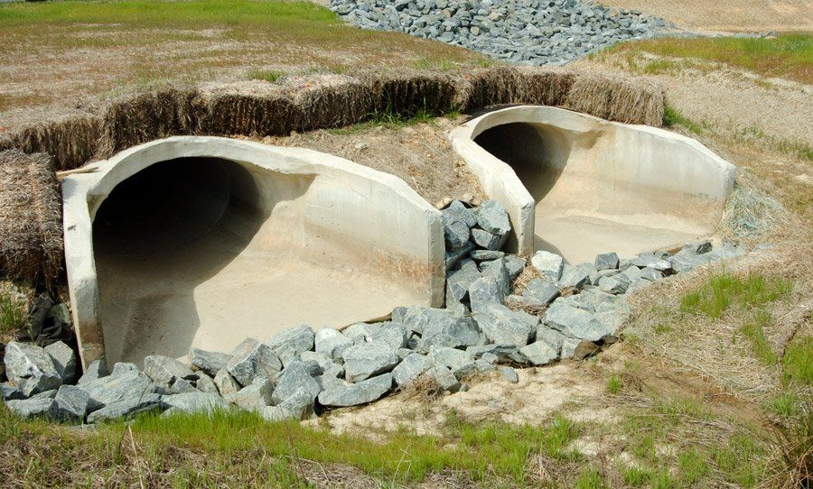 Two large concrete culverts with water runoff in a rocky grassy ditch
