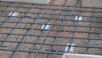 Steel rebar grid laid over compacted dirt at a construction site, with white spacers between bars