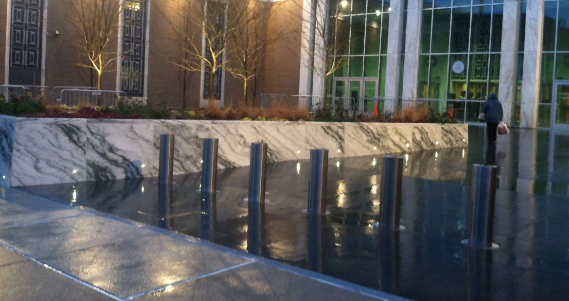 Modern building entrance with marble walls and reflective glass, bordered by dark water pools at dusk