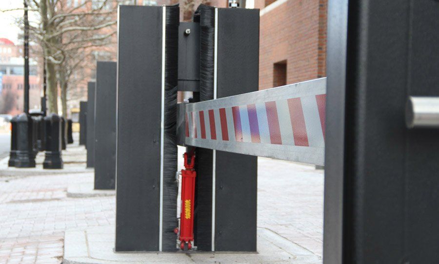 Parking barrier with red reflective stripes blocking a sidewalk between black posts