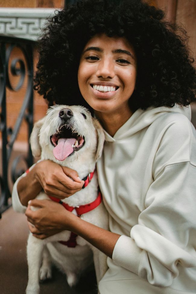 Person holding a smiling dog in a light hoodie outdoors
