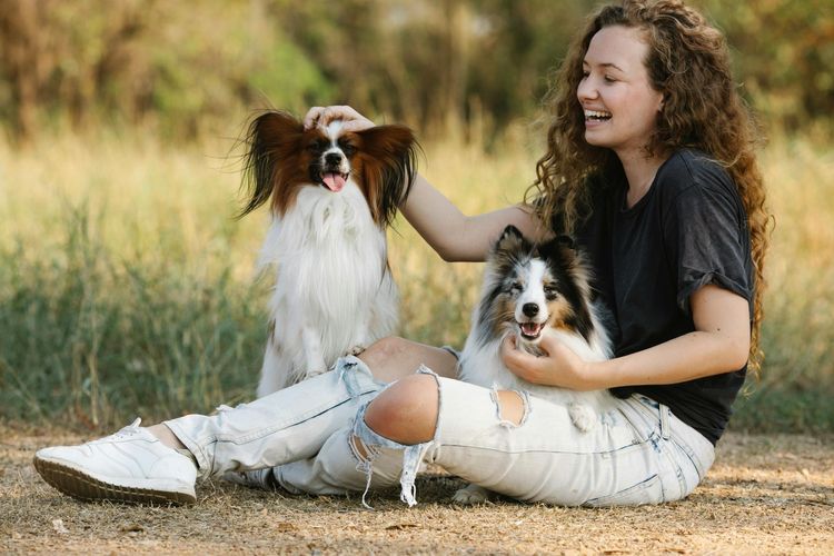 Woman sitting in grass with two small dogs, smiling in a sunlit field