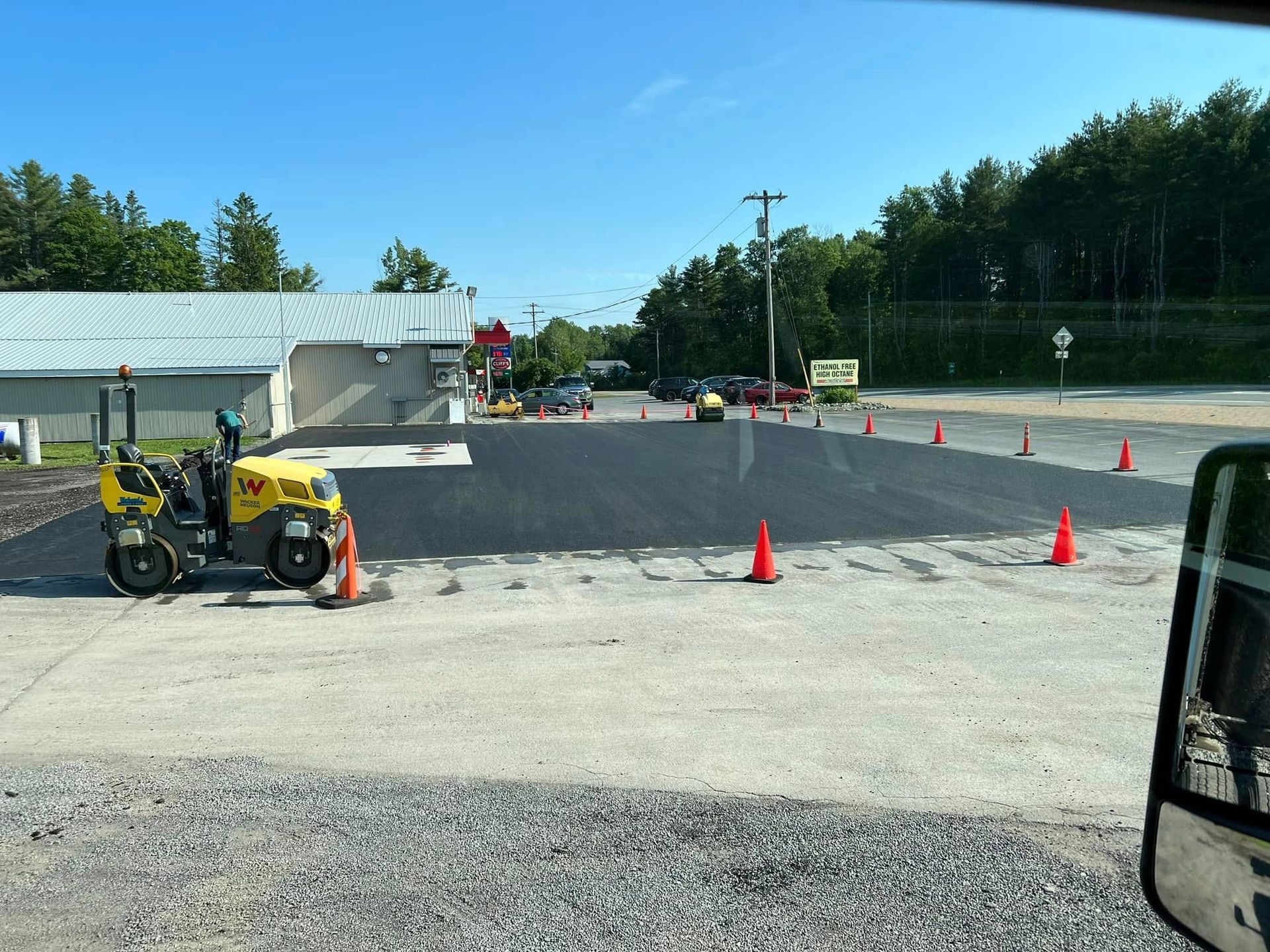 Roadwork scene with cones and a yellow paving machine on a newly paved section of road.