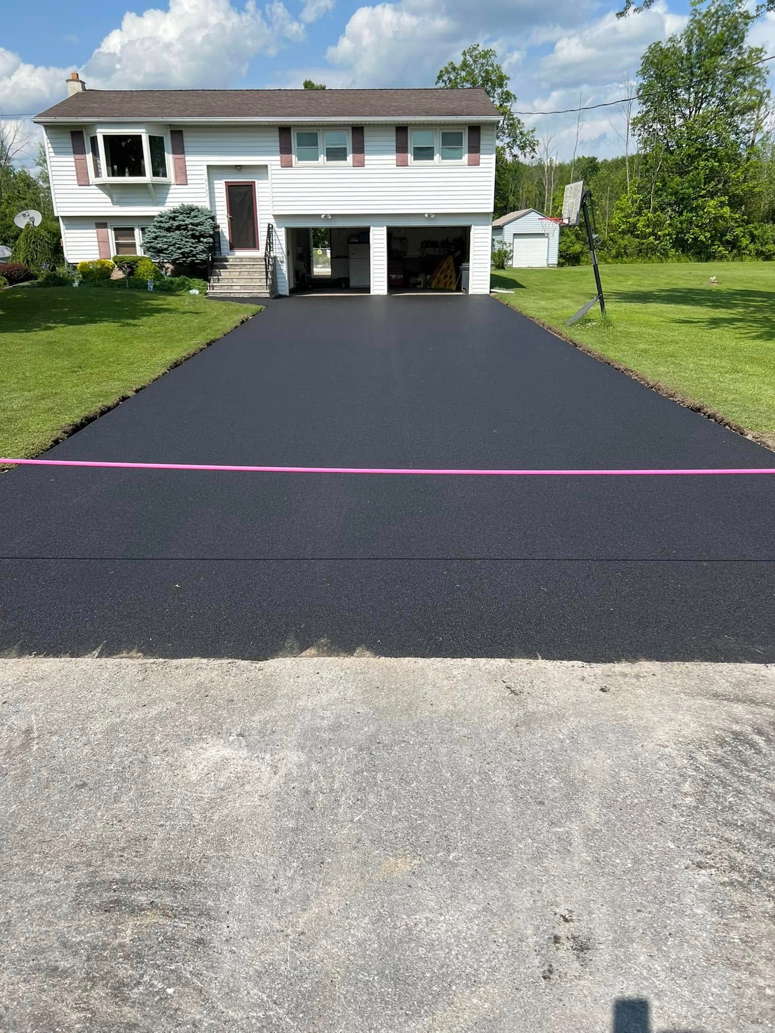 Two-story house with a newly paved black driveway and attached garage under a blue sky