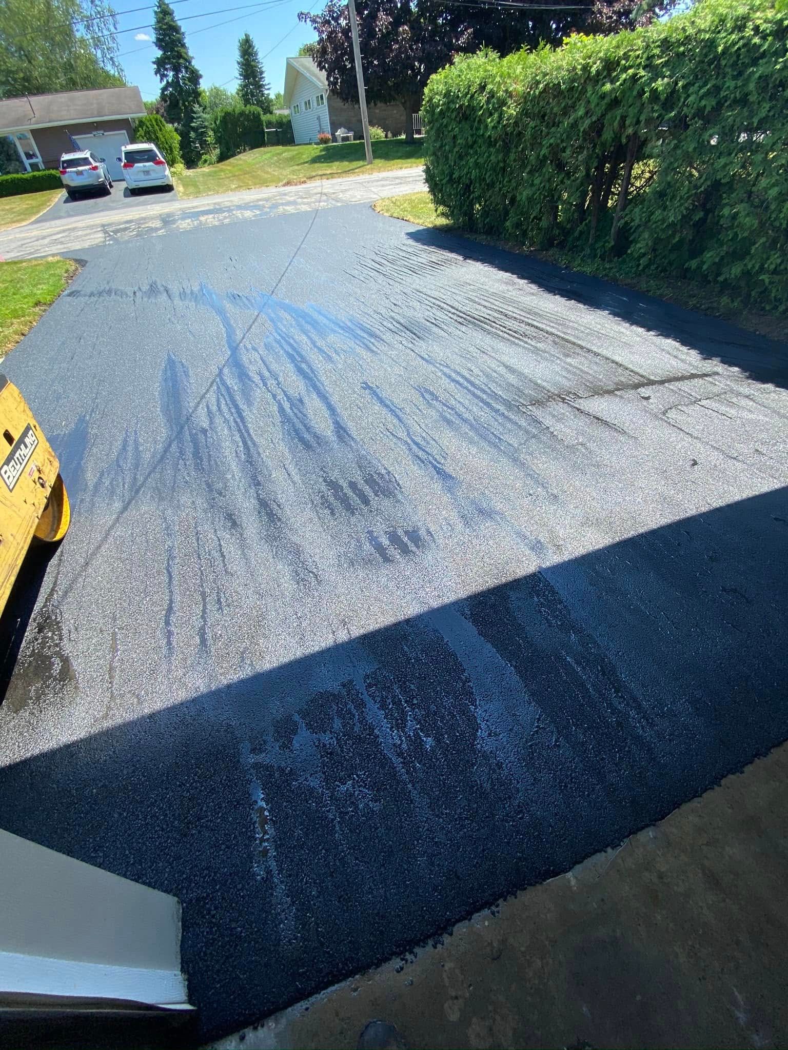 Gravel driveway with blue markings, bushes on the right, and parked vehicles in the distance.