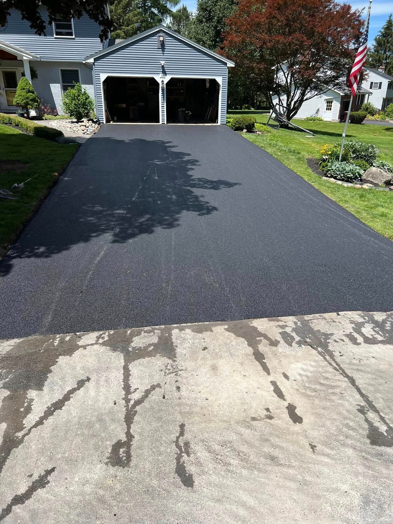 Fresh black driveway leading to a white garage in a suburban home yard