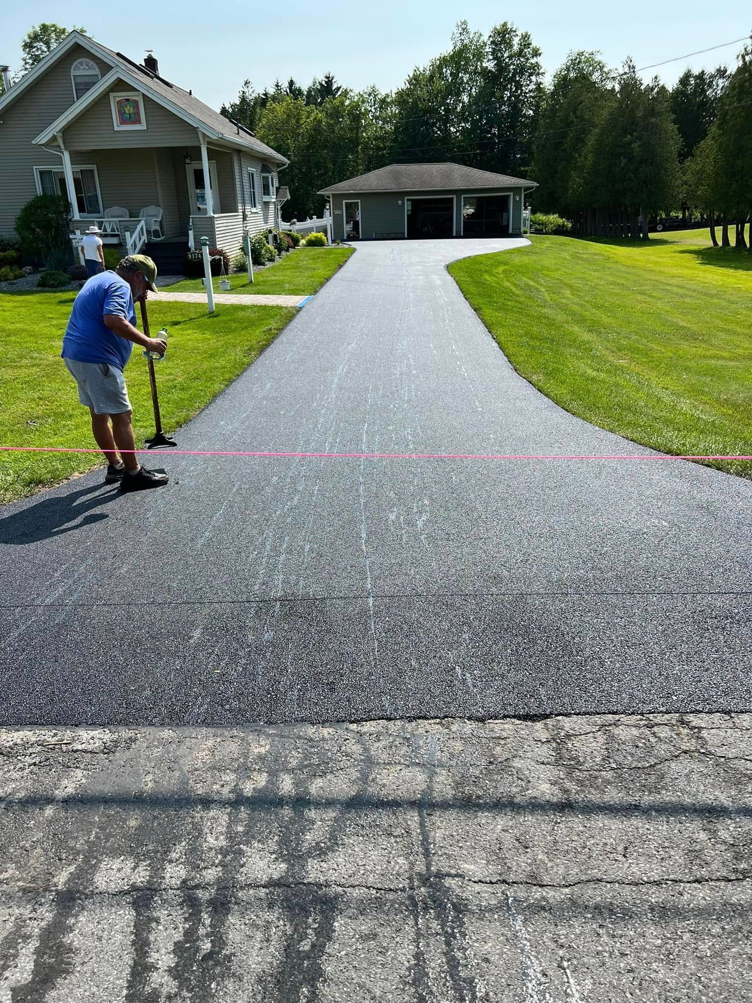 Person using a measuring tool on a newly paved driveway beside a house and lawn.