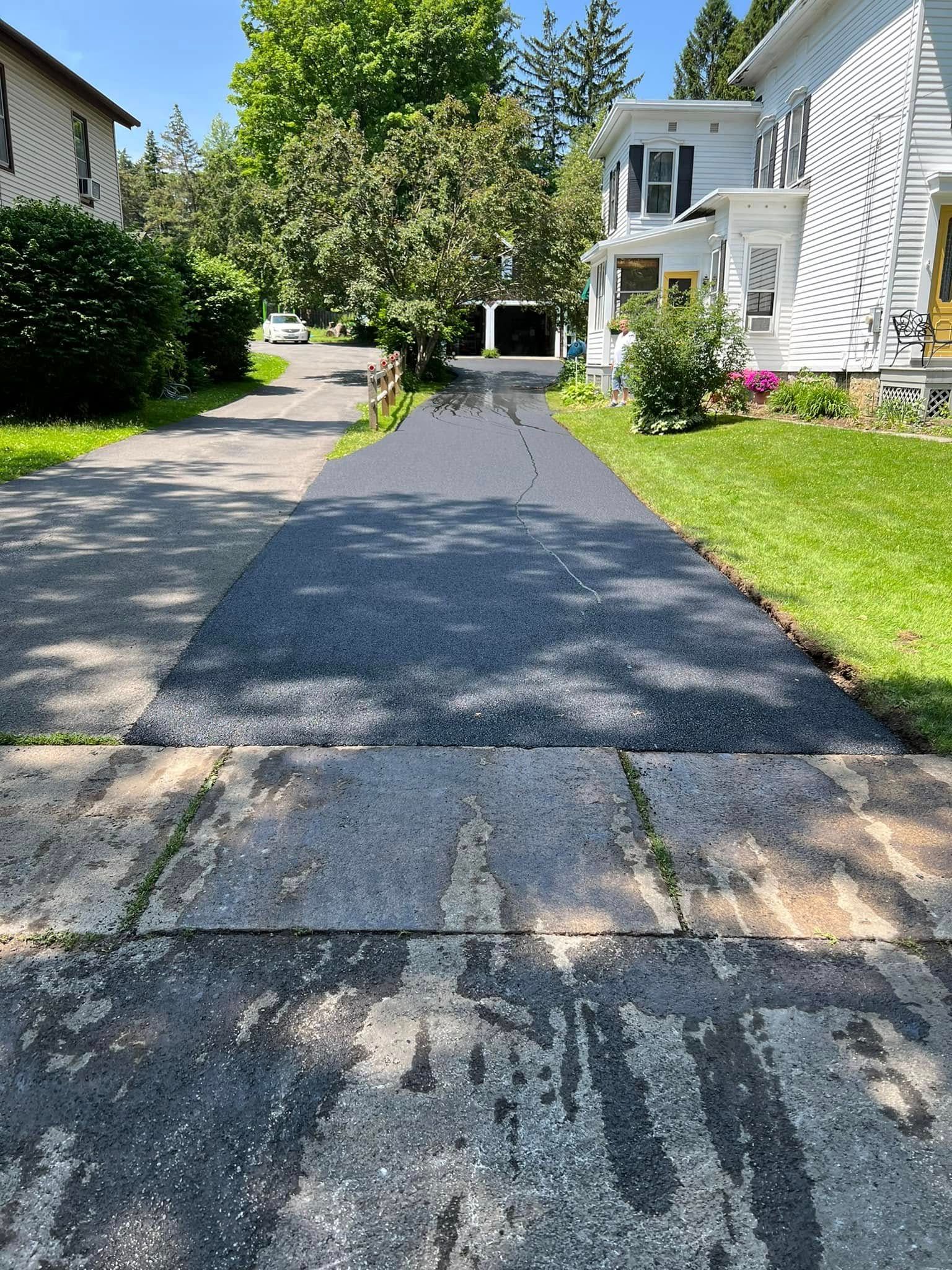 Driveway leading to a white house, with trees and green lawns on both sides.