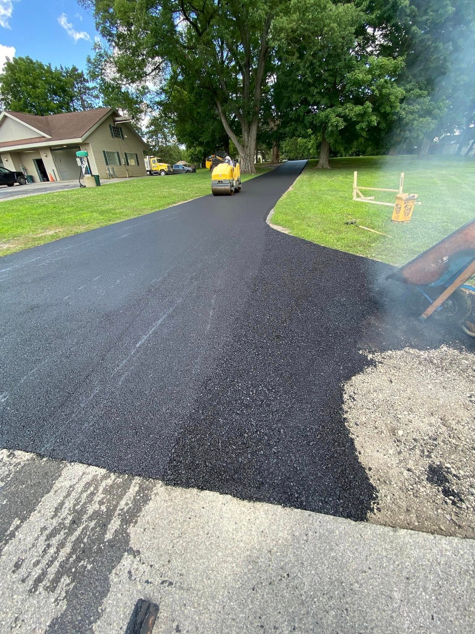 Freshly paved black driveway with a yellow roller and a house in the background