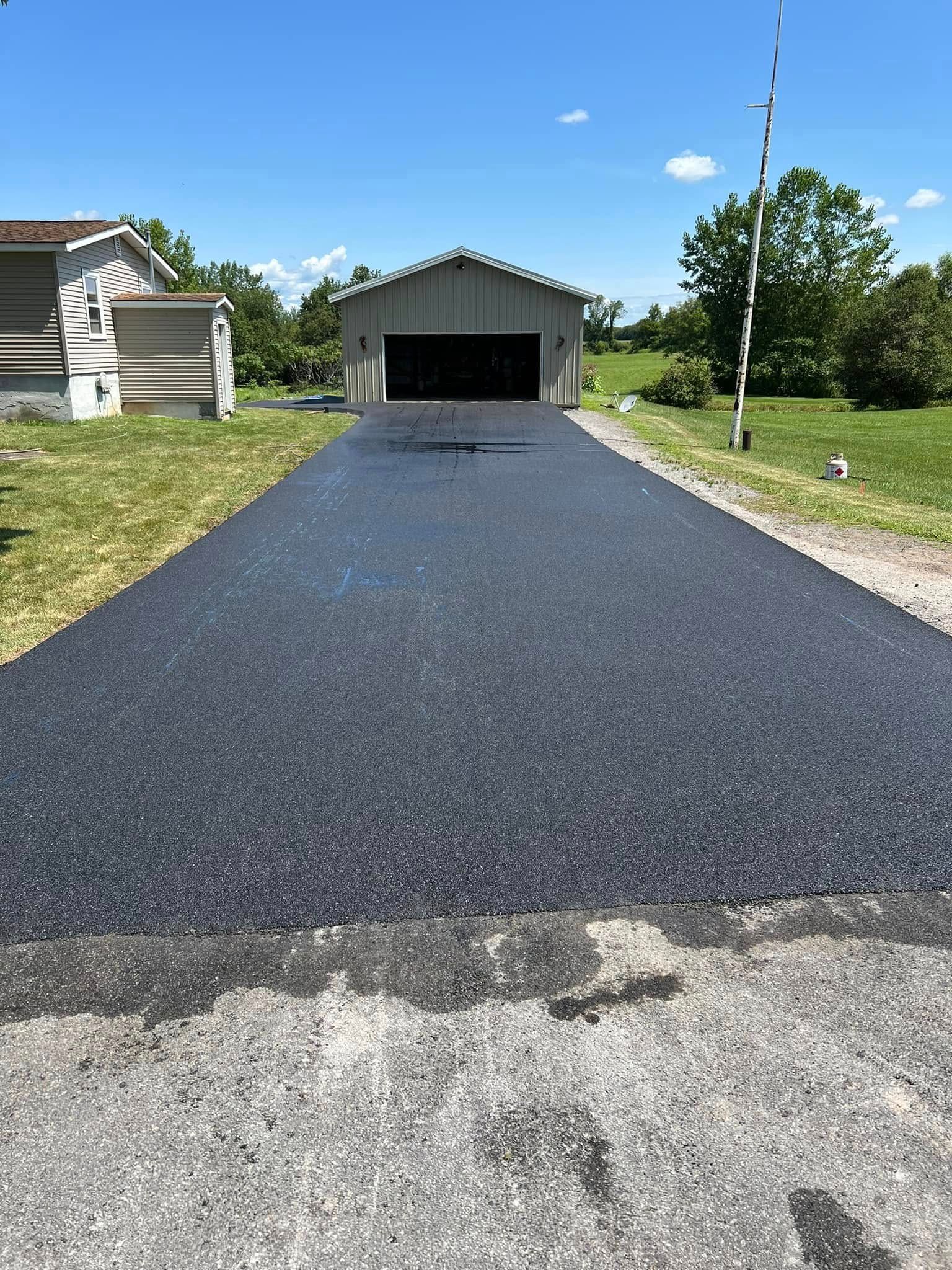 Freshly paved black driveway leading to a garage on a sunny residential property