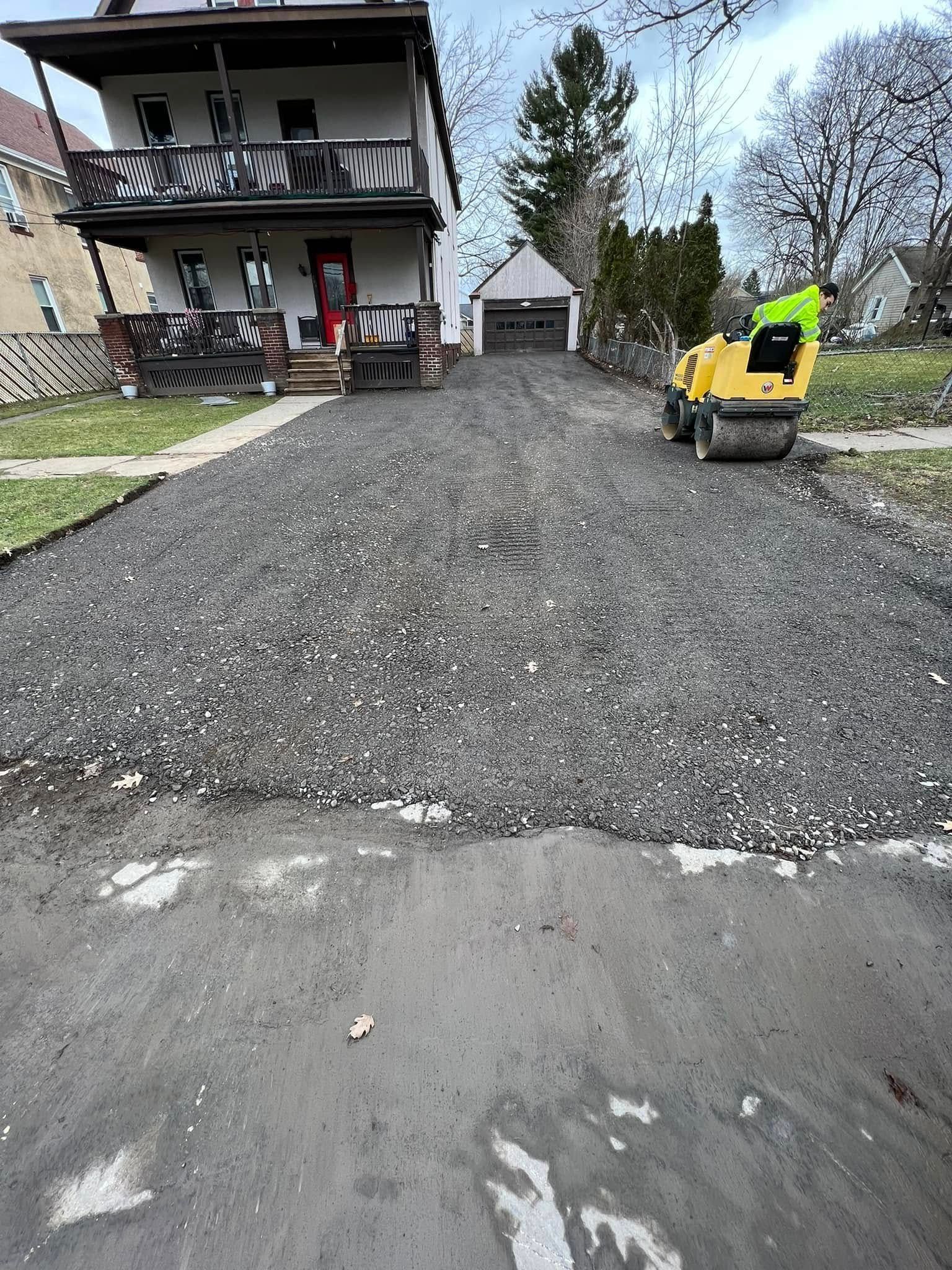 Gravel driveway leading to a house and garage, with a yellow construction machine on the right.