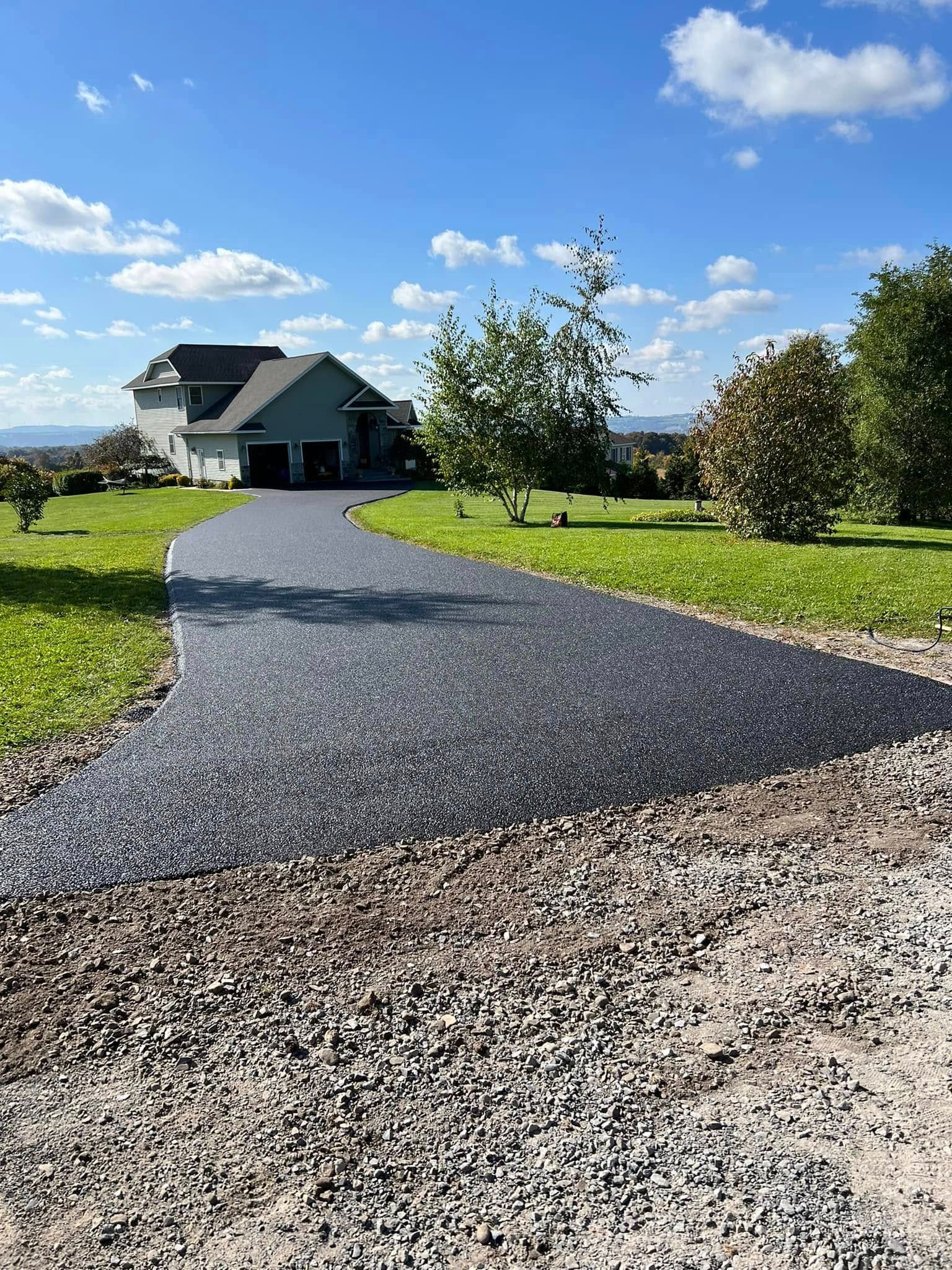 Gravel driveway leading to a gray house on a sunny green lawn under a blue sky.