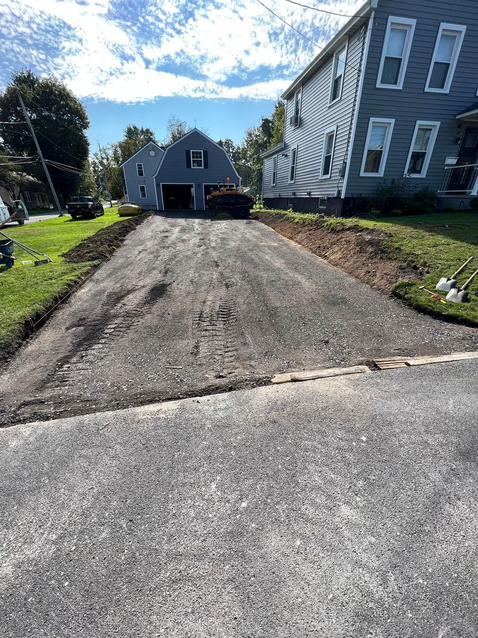 Rough gravel driveway leading to a gray house on a sunny day