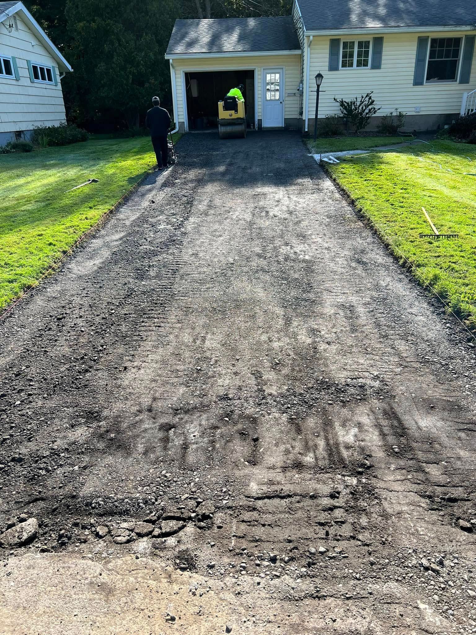 Freshly graded gravel driveway leading to a garage, with a worker in a hi-vis vest at the entrance