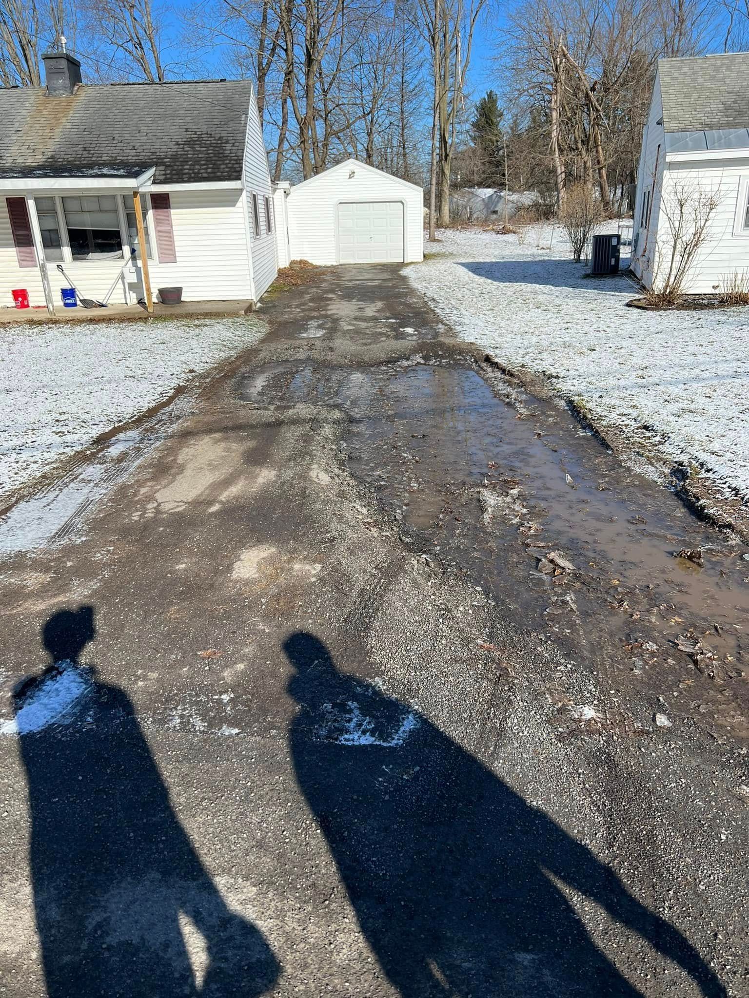 Snowy driveway leading to a white garage, with two long shadows in the foreground.