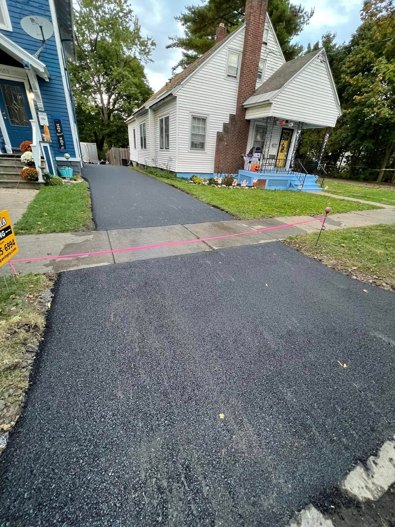 Paved walkway leading to a damaged white house with blue trim and pink caution tape across the path