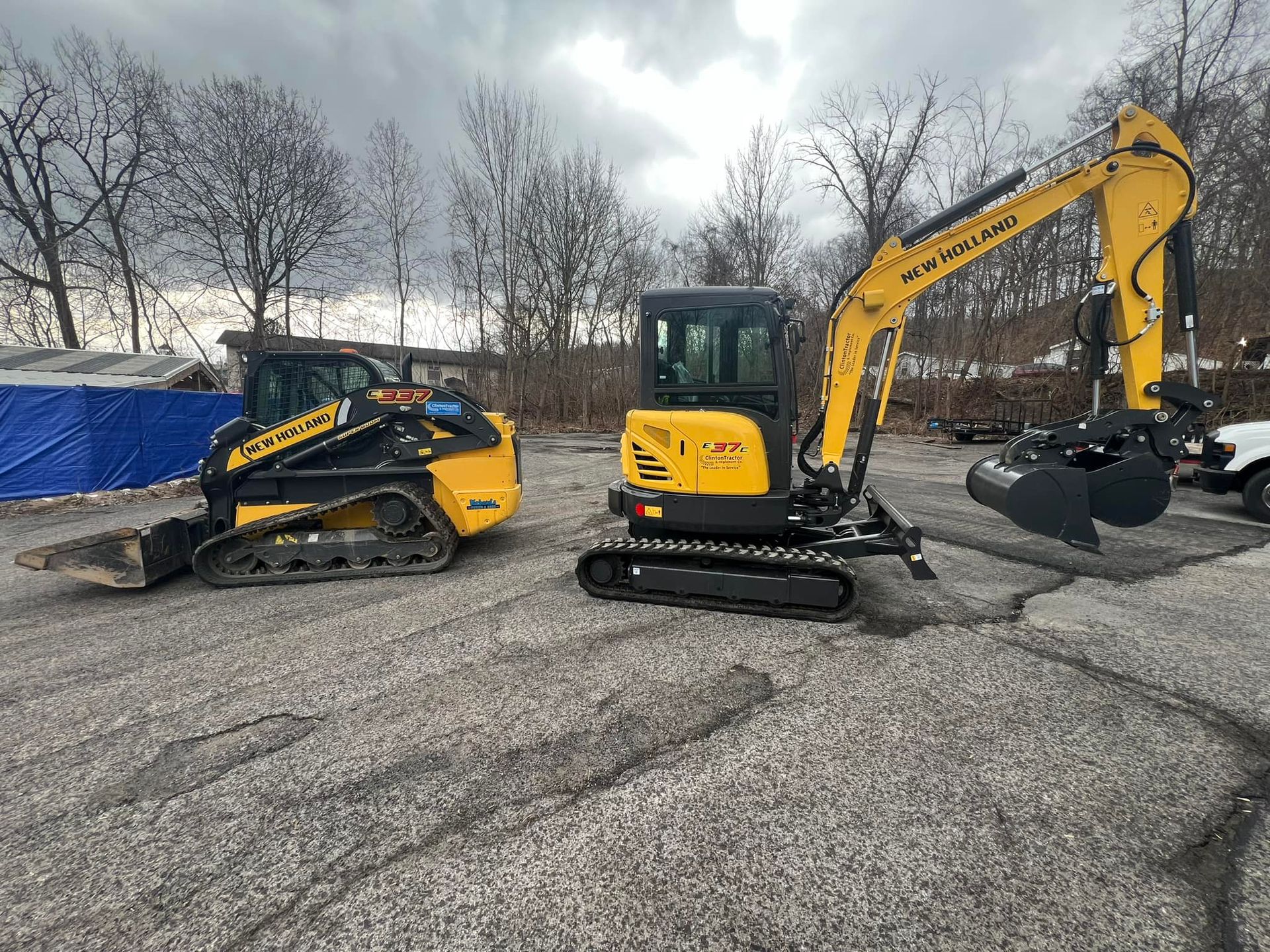 Two yellow mini excavators parked on a gravel lot under a cloudy sky