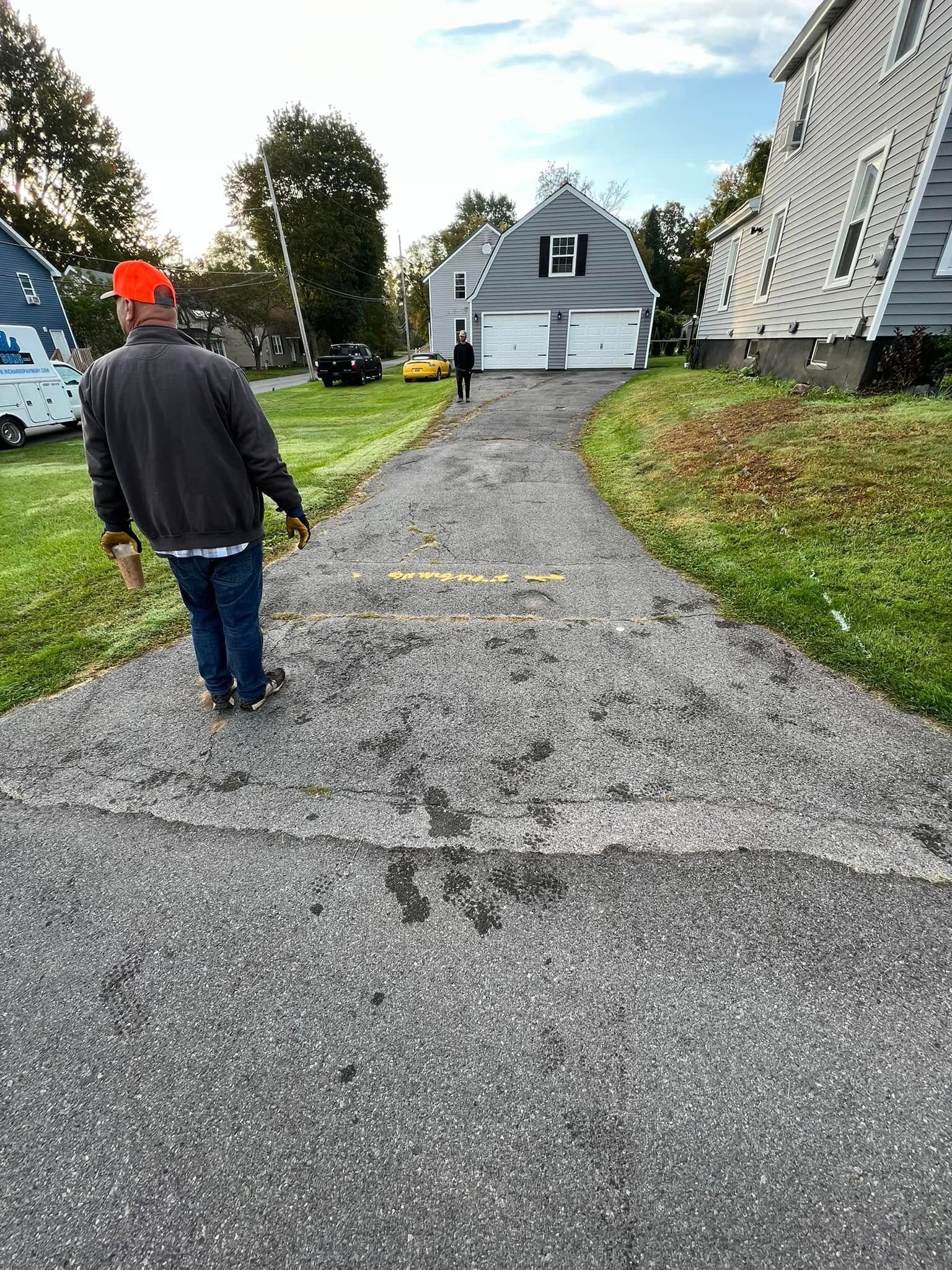 Person walking on a gravel driveway toward a white house on an overcast day.