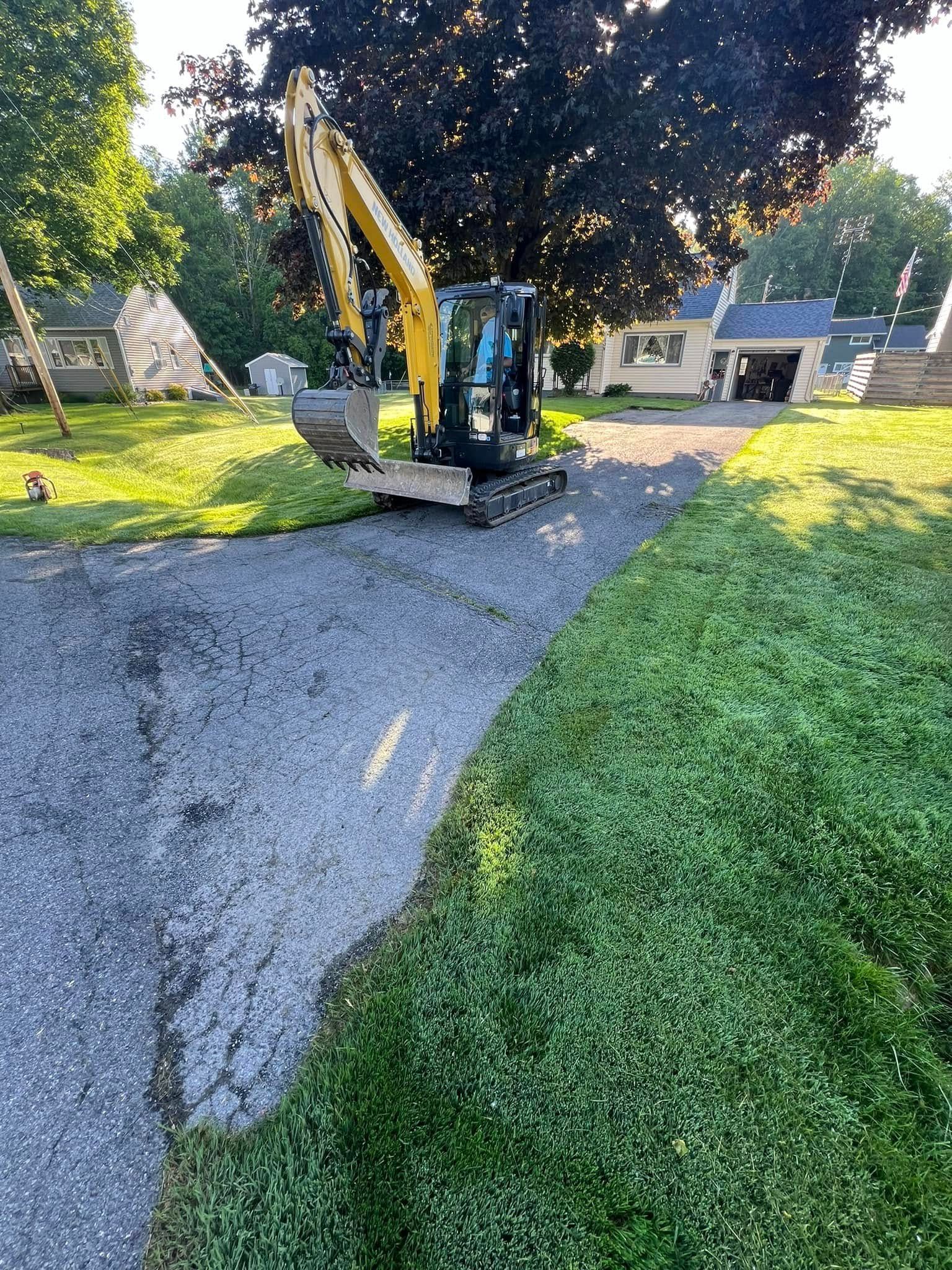 Excavator on a gravel path beside a grassy yard with a tent and house in the background