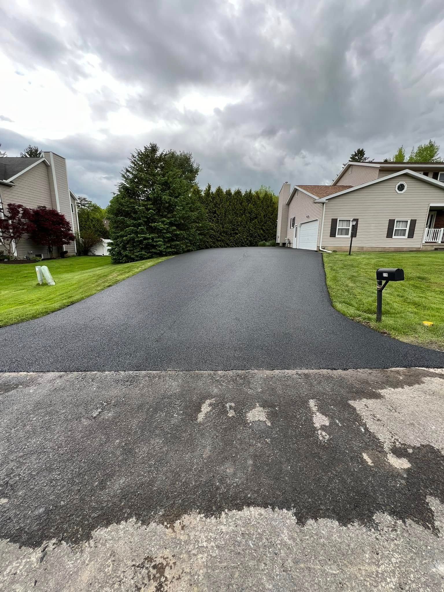 Fresh black asphalt driveway between suburban houses under cloudy skies