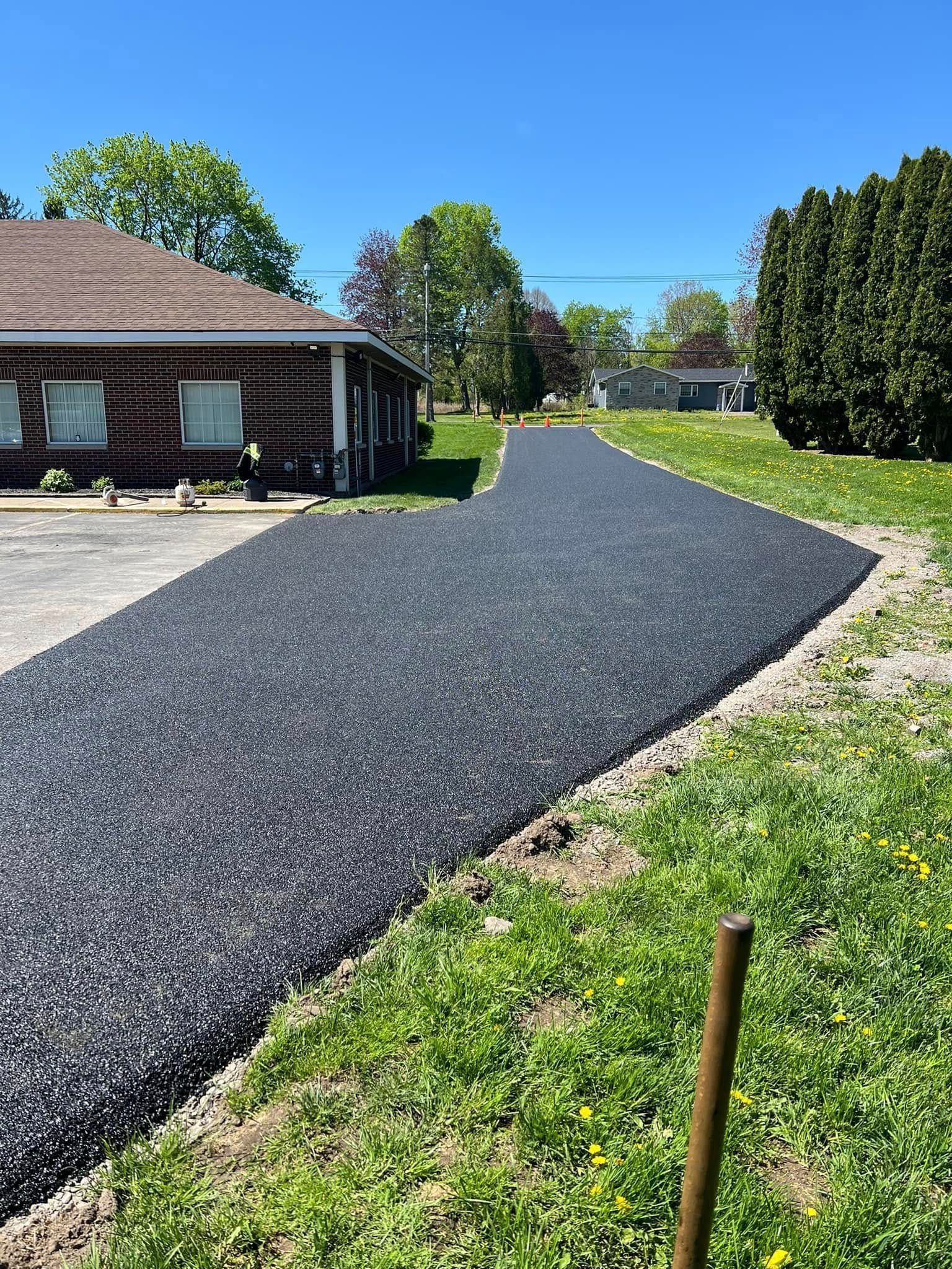 Fresh black gravel driveway curving past a house on a sunny day