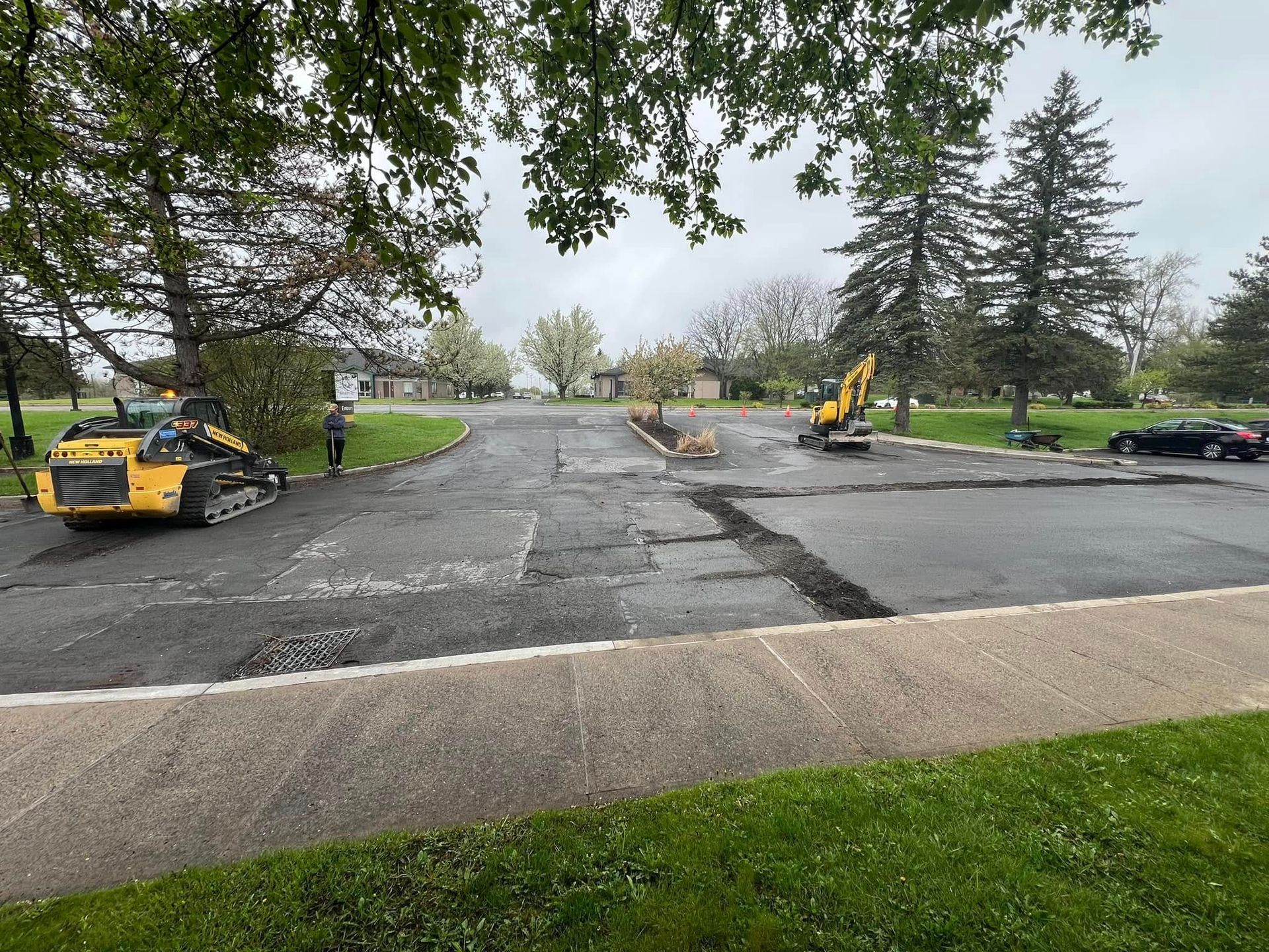 Road paving work with two yellow construction machines on a tree-lined street in a park-like area