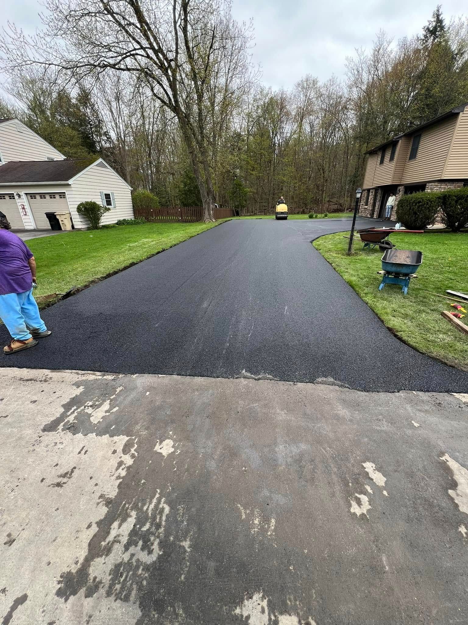 Freshly paved black driveway between houses, with a child in purple at left and landscaping along the sides