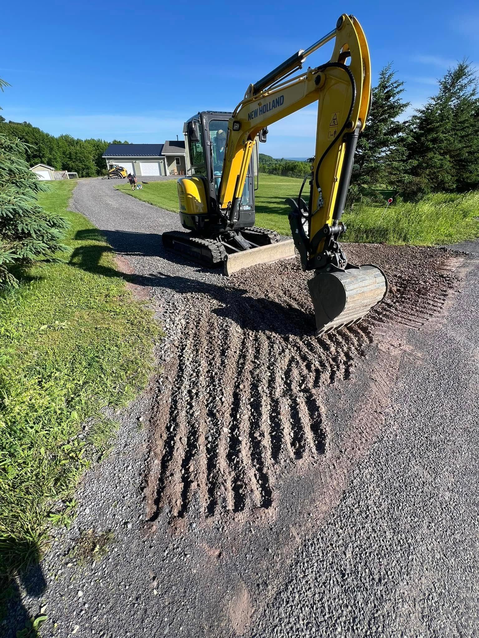 Yellow excavator spreading gravel on a driveway under a clear blue sky