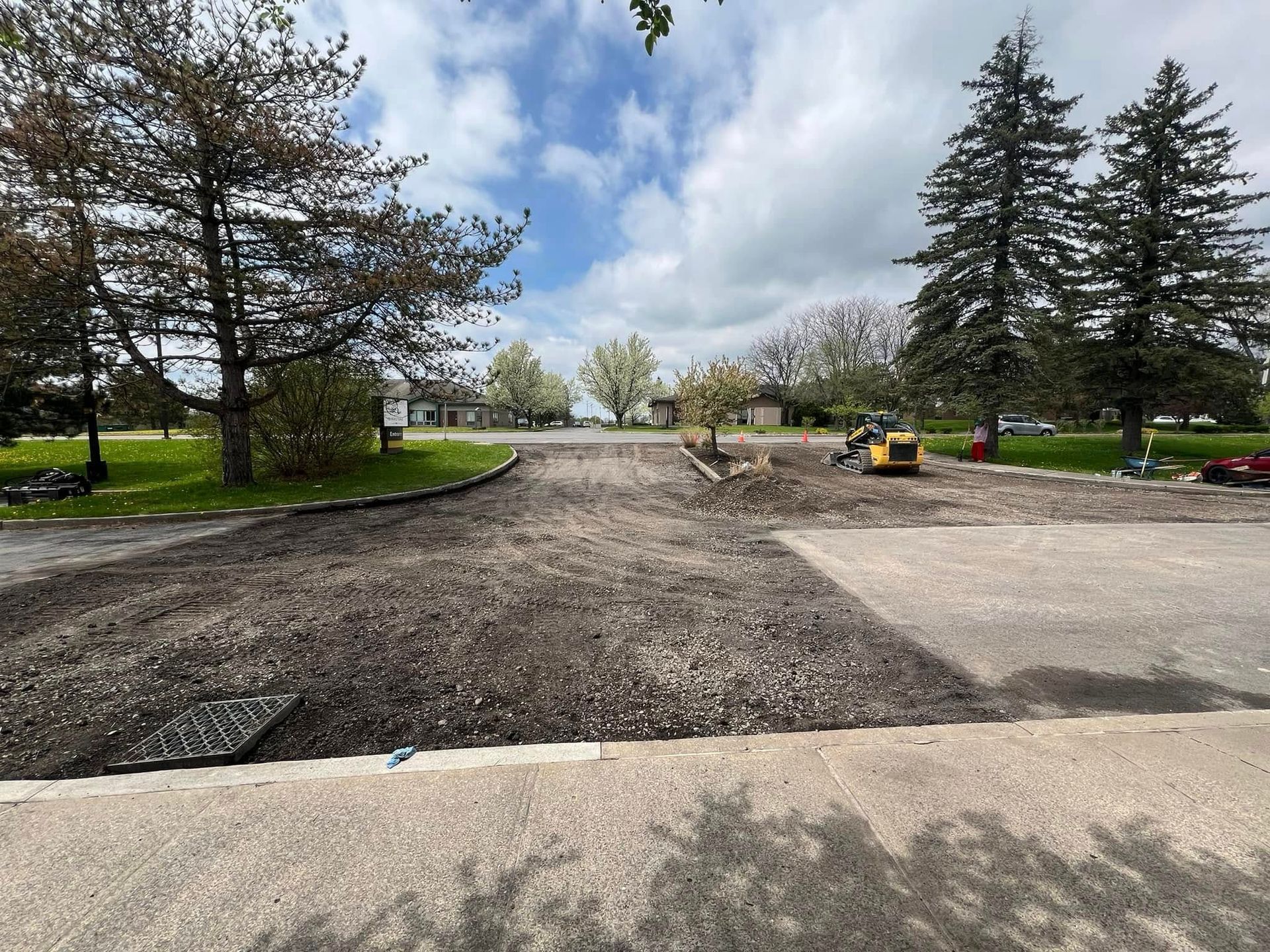 Wide parking lot under construction with fresh gravel, trees, and a cloudy sky
