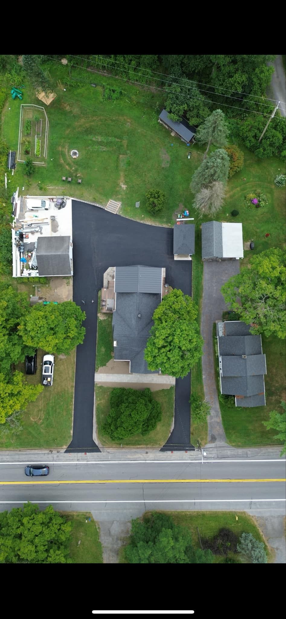 Aerial view of a house with driveway, yard, and road at the bottom