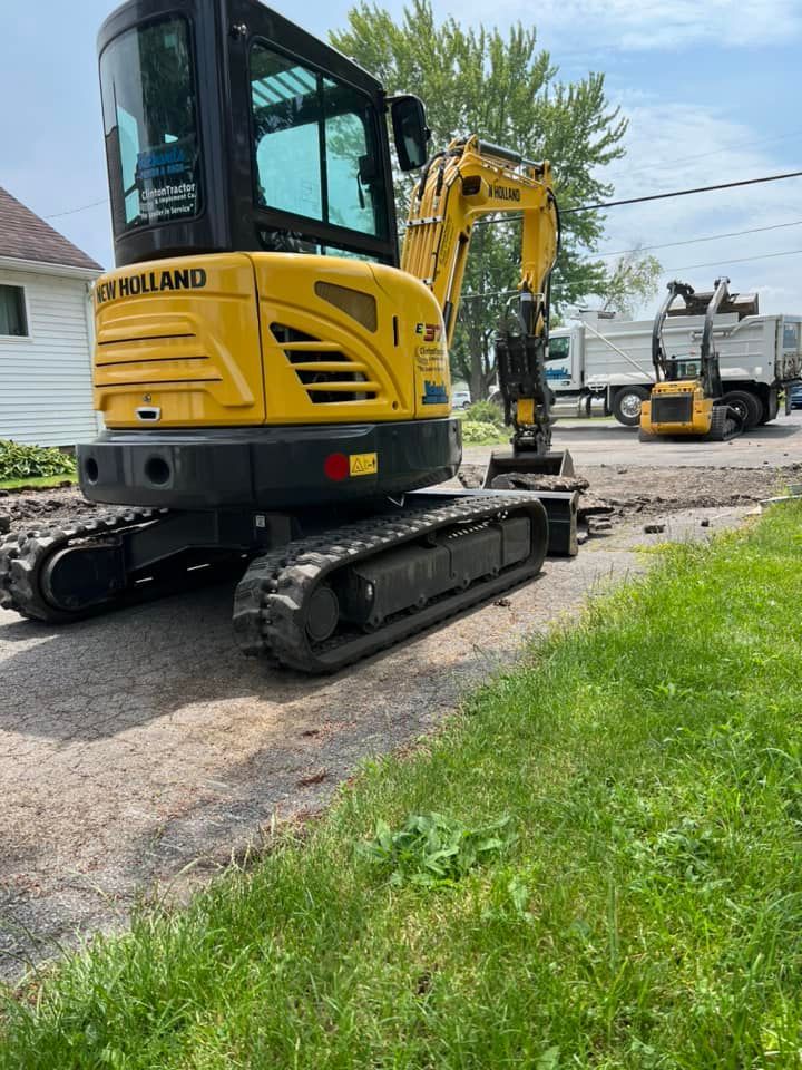 Yellow excavator on a gravel driveway beside a house, with another excavator in the background.