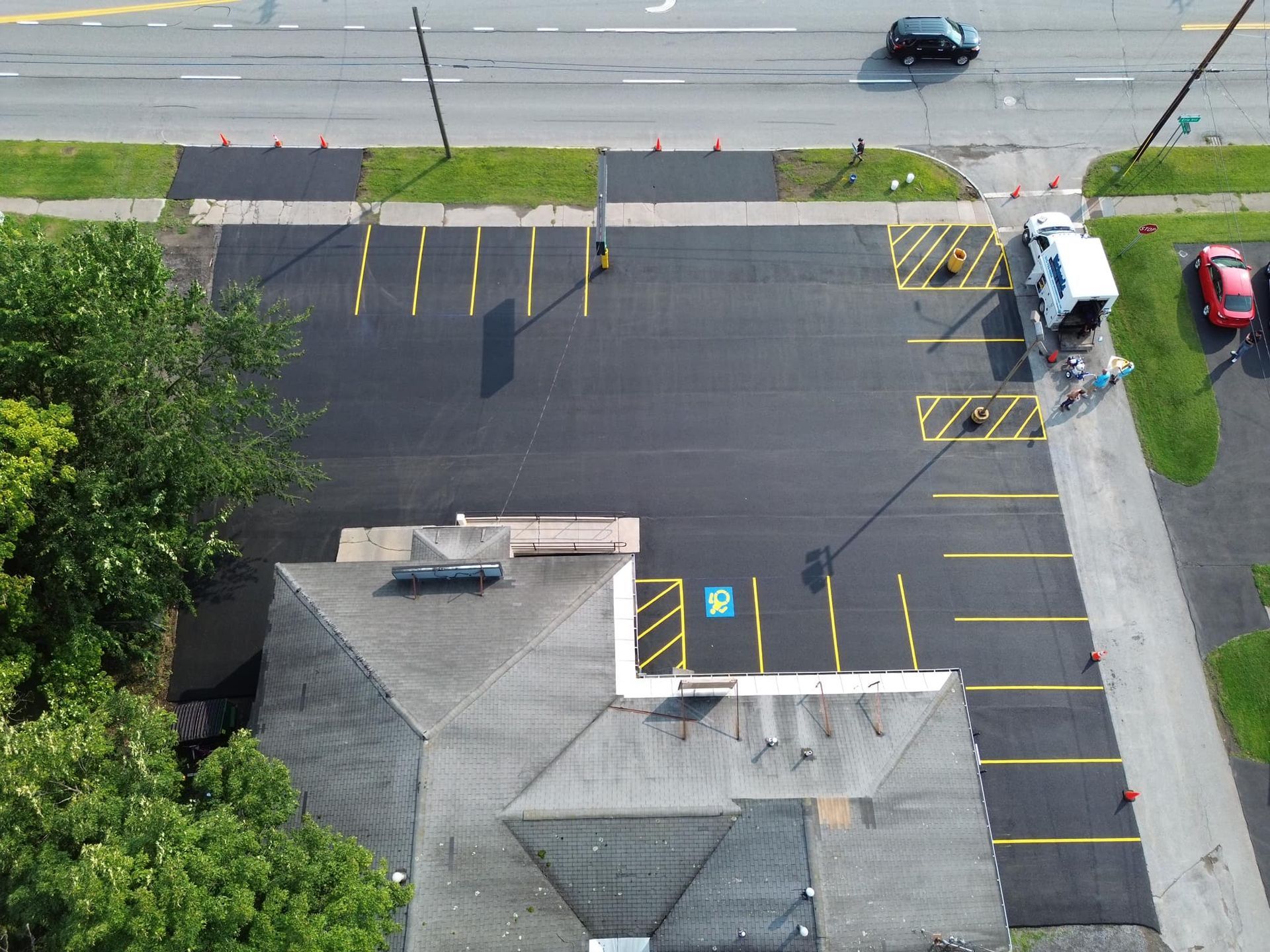 Aerial view of a mostly empty parking lot beside a street, with yellow striped accessible spaces and parked cars.