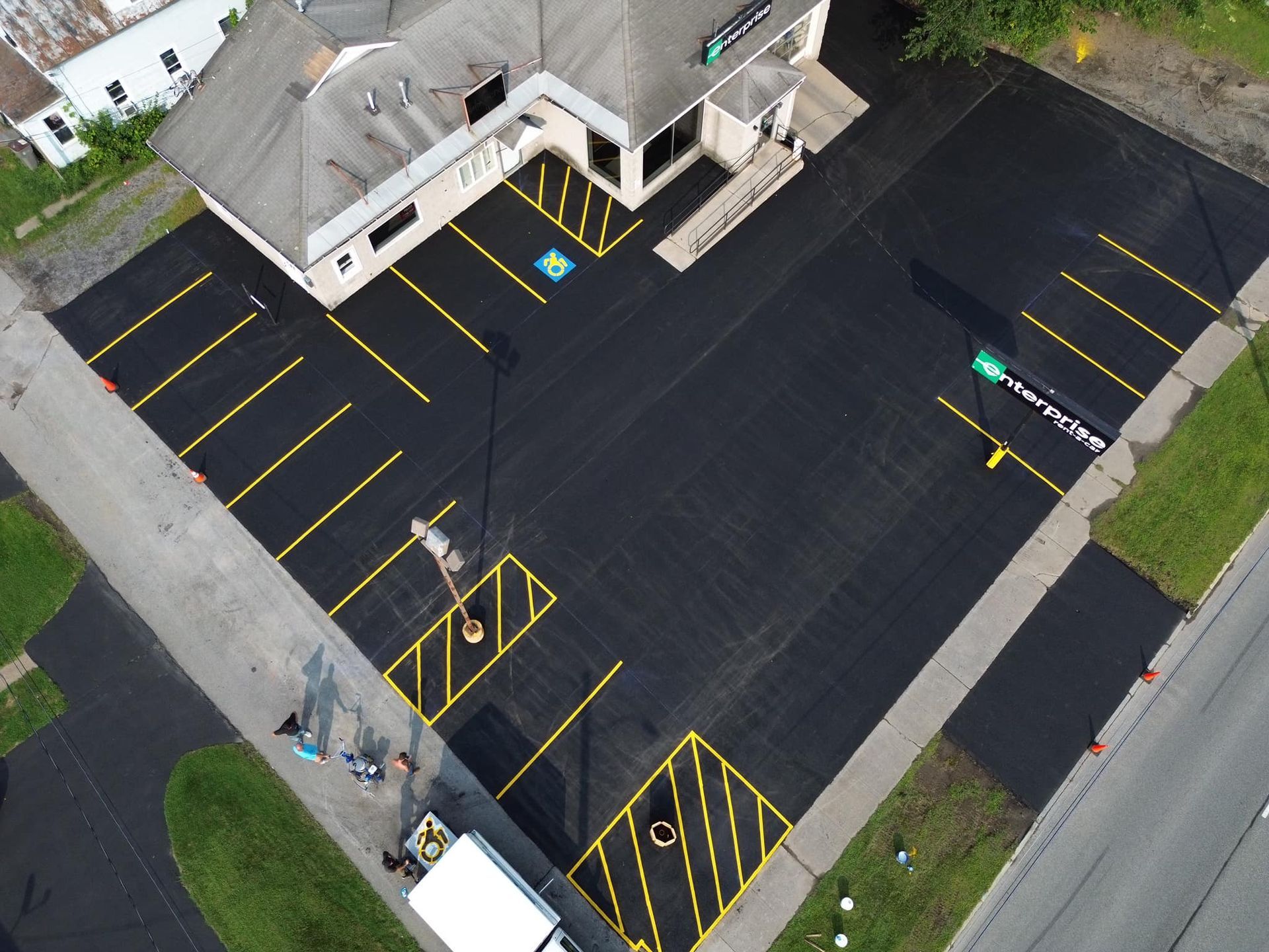 Aerial view of an empty parking lot with yellow lines beside a building and sidewalk