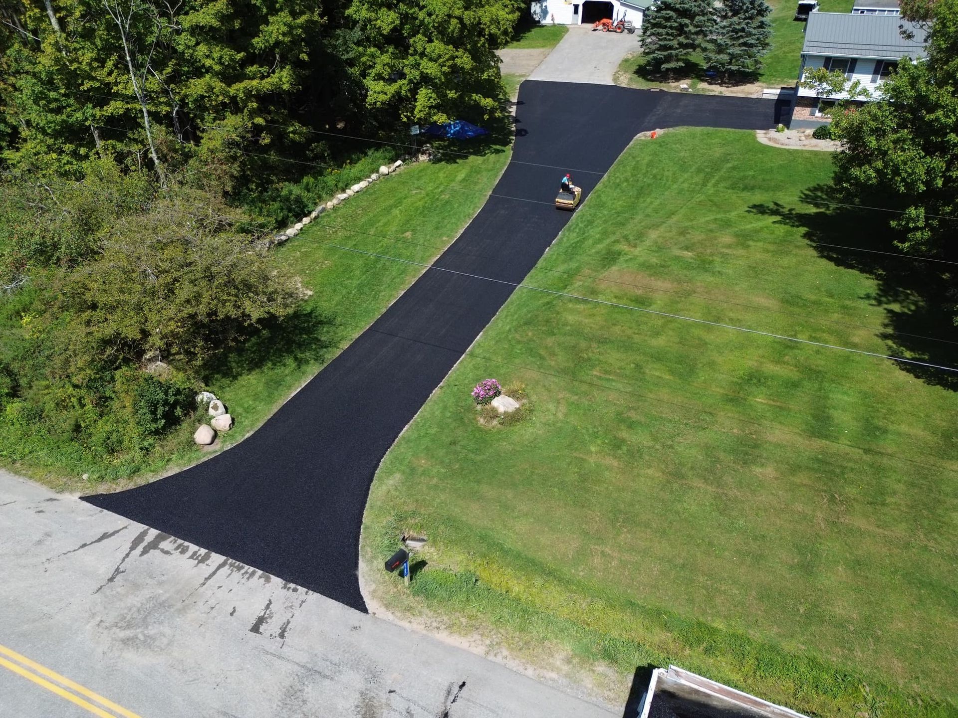 Fresh blacktop driveway winding through a green lawn toward houses and trees