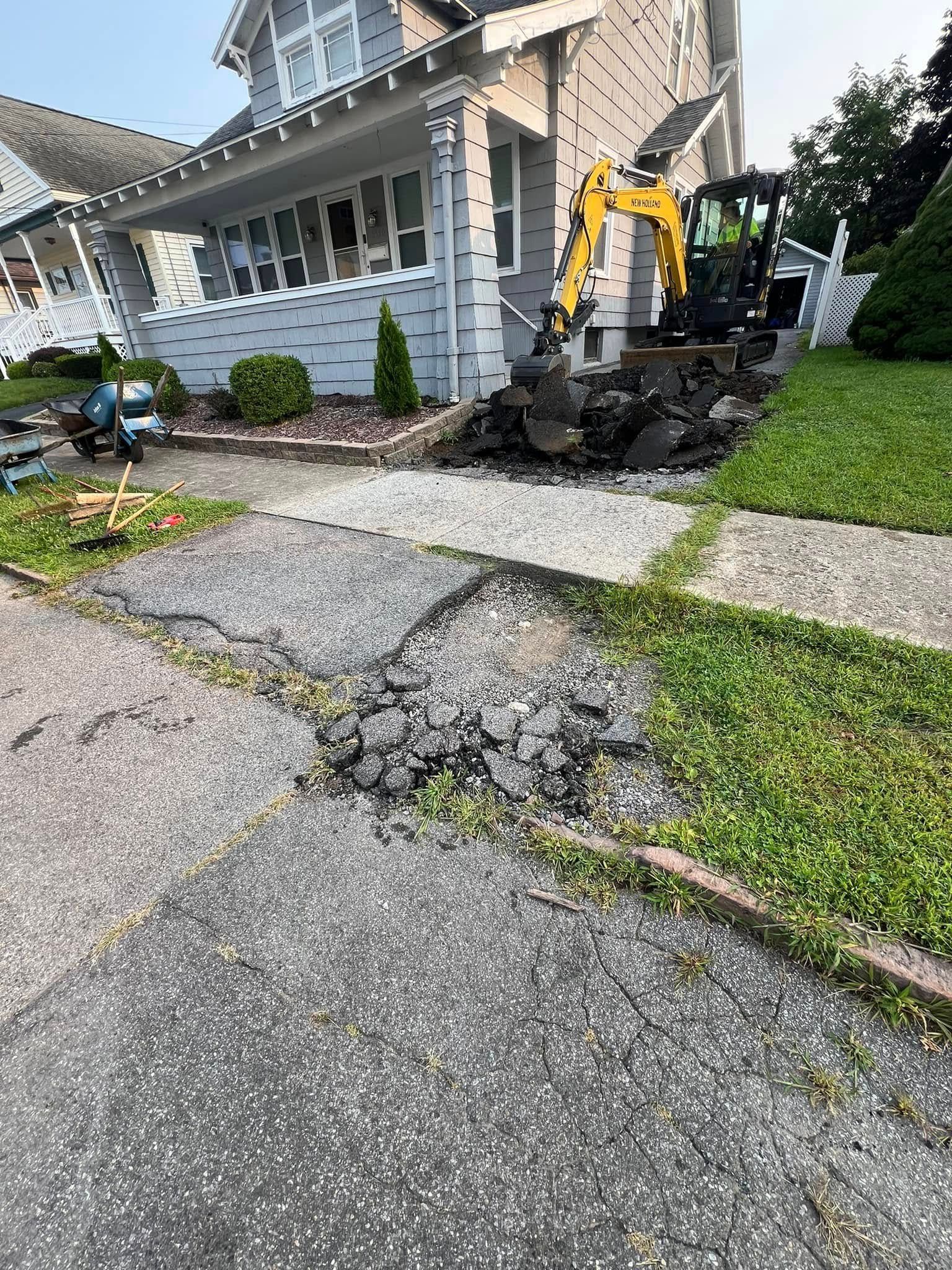 House front with a yellow excavator and broken cracked sidewalk in a residential yard