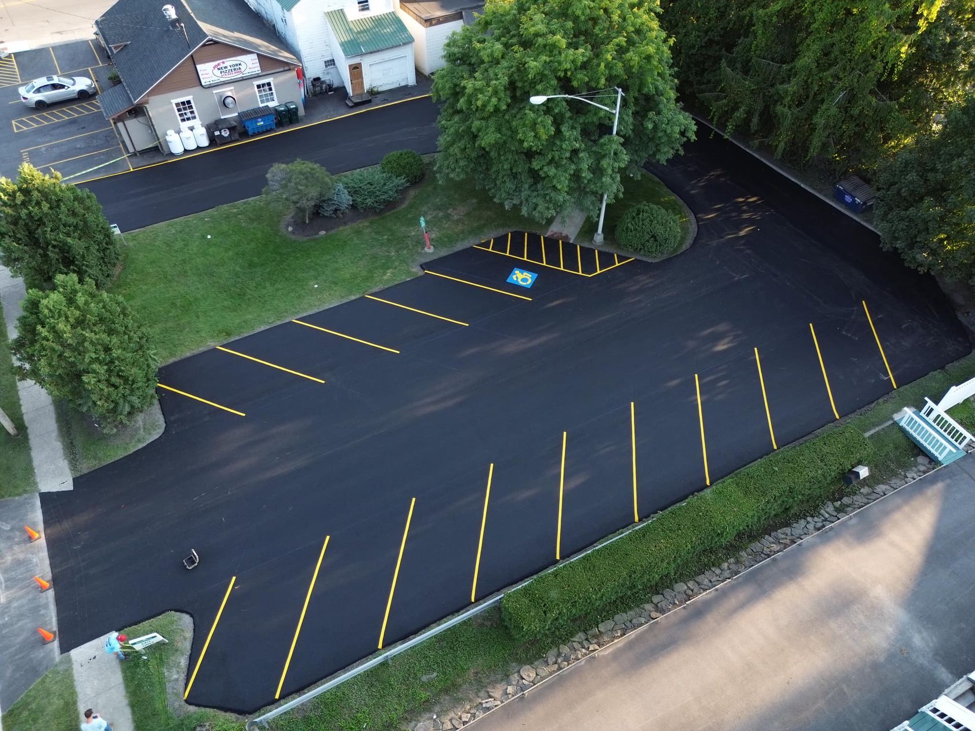 Aerial view of an empty blacktop parking lot with yellow lines beside trees and a road