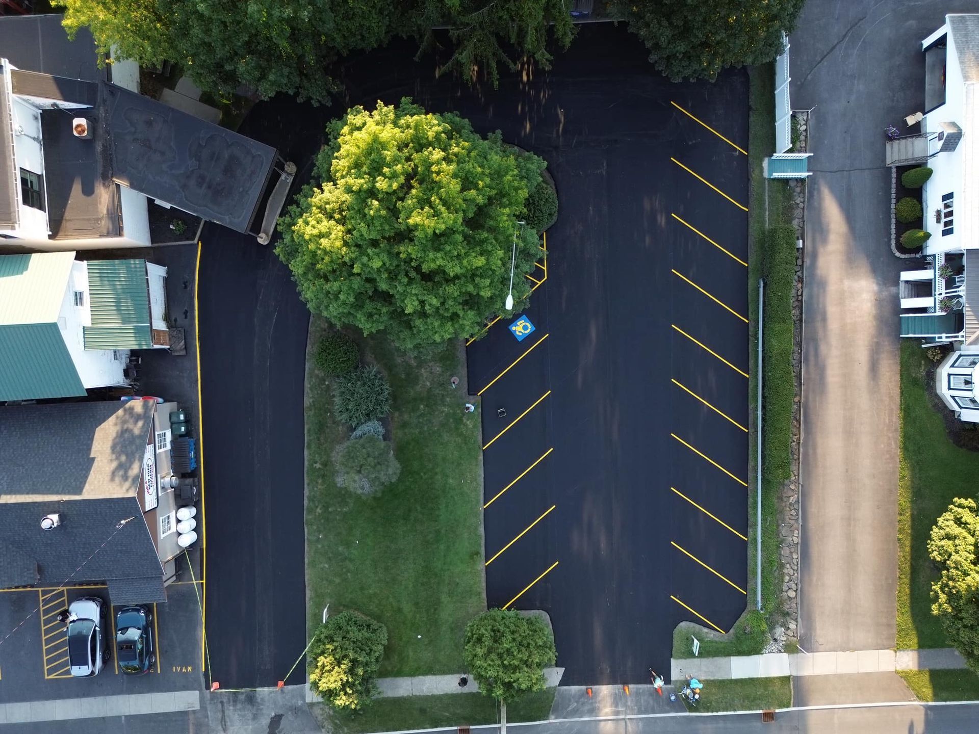 Aerial view of a parking lot with yellow-striped spaces, trees, and adjacent buildings.
