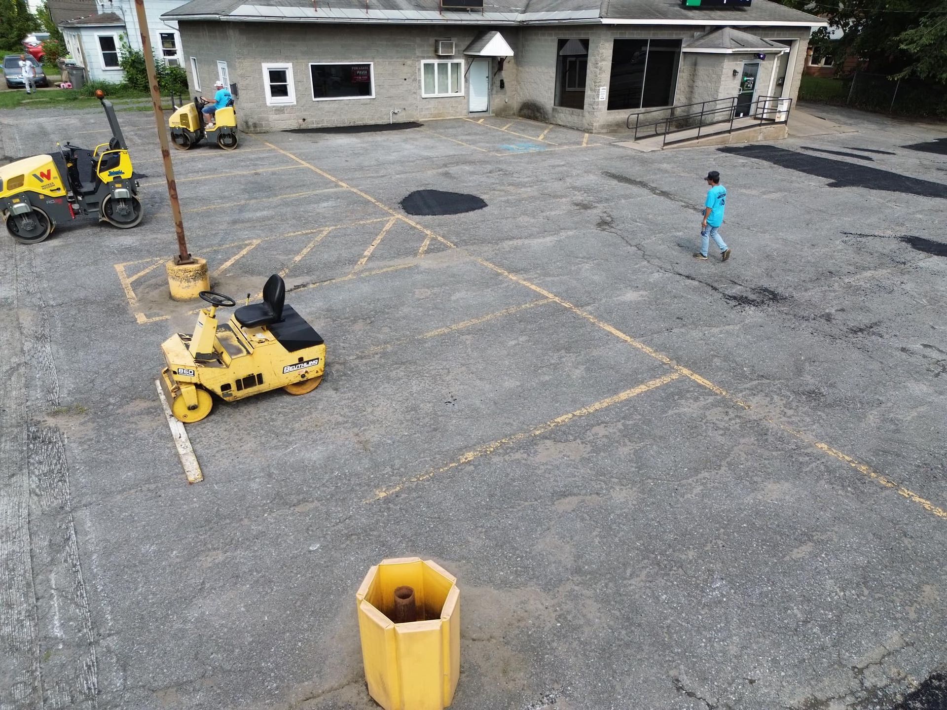 Construction site with yellow road roller, workers, and a gray building in the background