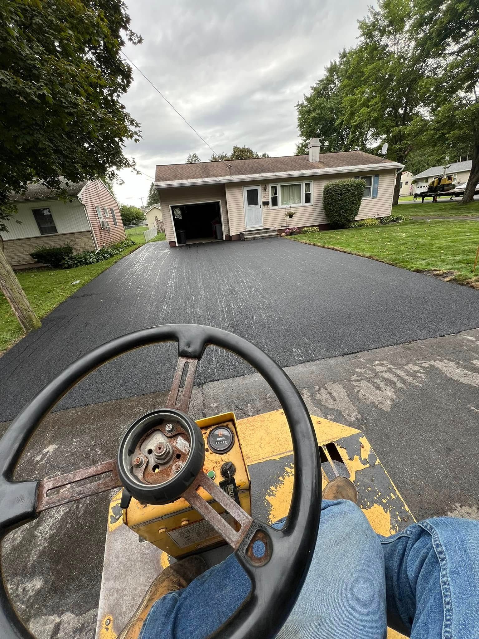 Riding a lawn mower up a freshly paved driveway toward a house and garage