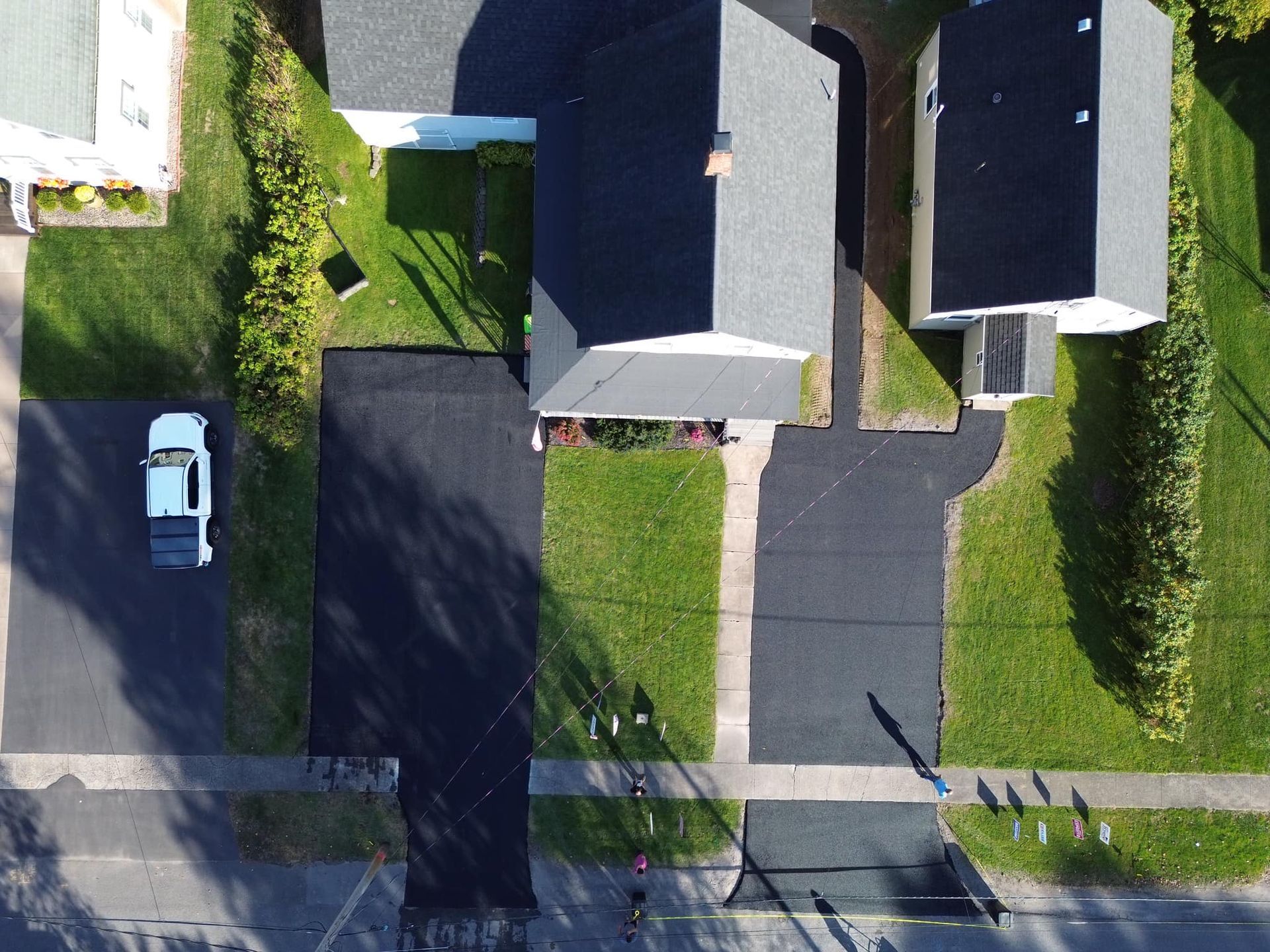 Aerial view of suburban homes, driveways, lawns, and a white car parked on the street.