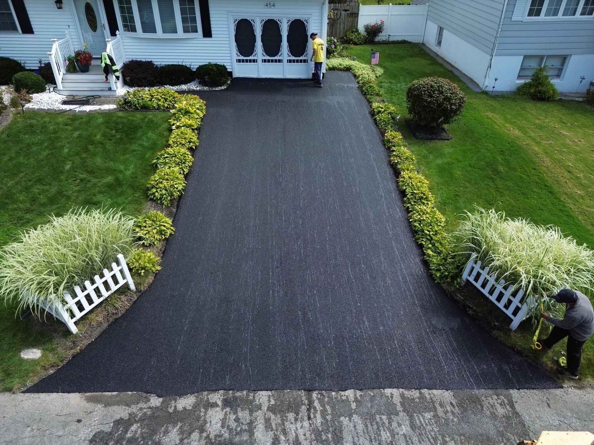 Long black driveway leading to a house with white railings and green lawn borders